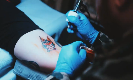 Close up of artist giving an owl tattoo.