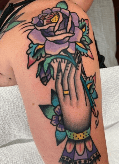 Tattoo of a woman's hand holding purple flower.