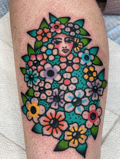 Tattoo of a woman's face hiding in a bed of colorful flowers.