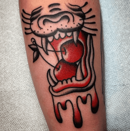 A tattoo of a lion's mouth about to bite into two cherries.