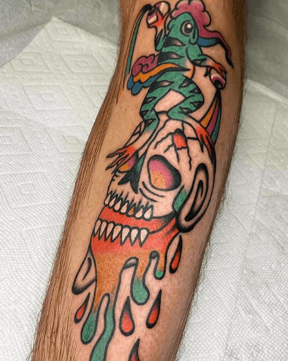 A tattoo of a frog holding two human eyeballs on top of a skull.