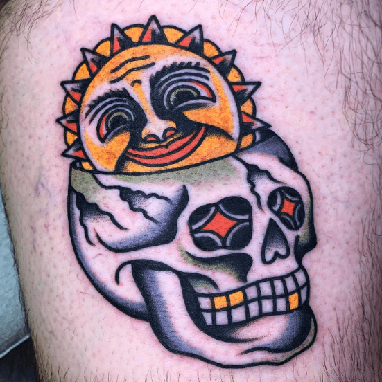 A tattoo of smiling sun rising out of a human skull.